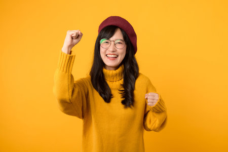 Happy young asian woman in yellow sweater and beret on yellow backgroundの写真素材