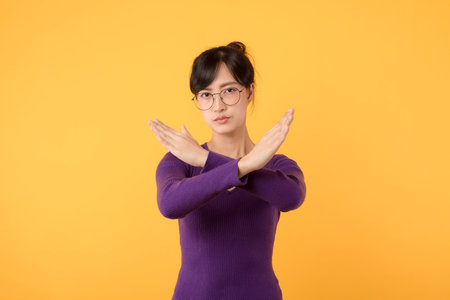 Young Asian woman making stop gesture with both hands on yellow background.の写真素材