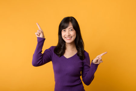 Get expert shopping advice from a cheerful young Asian woman in her 30s wearing purple shirt isolated on yellow background. here to help for choose the best with smile. Explore fashion tips concept.の写真素材