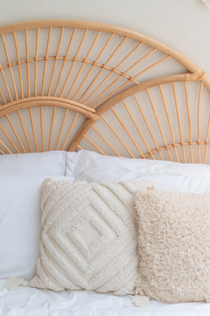 Detail image of a bedroom with woven brown wooden headboard with white wall and white and brown pillow.の写真素材