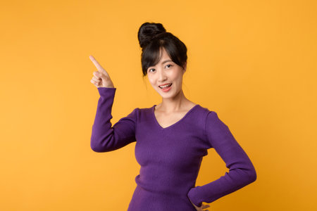 Smiling young asian woman in purple sweater on yellow background.の写真素材