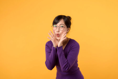 happy and cheerful teenage girl wearing purple shirt and eyeglasses, confidently posing with a pretty smile. Expressing emotions and positivity in a yellow background.の写真素材