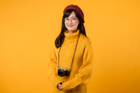 In her cheerful studio, young Asian woman, wearing a yellow sweater and red beret, snaps pictures with her camera, embracing the joy of photography.の写真素材