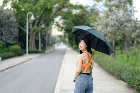 Protecting with flair, an Asian woman's vibrant umbrella adds joy to the sunny scene.の写真素材