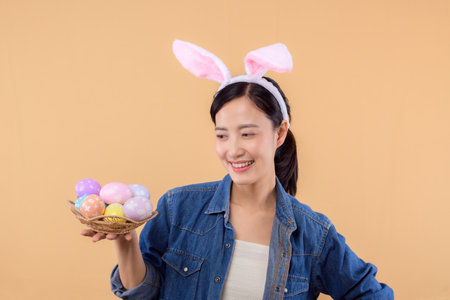 Portrait asian young woman wearing denim clothes and bunny rabbit ears and holding colorful eggs...