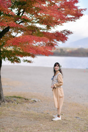 Asian woman in casual dress embraces the fall beauty of Japan, enjoying holiday filled with smiles, fashion, and vibrant foliage. A cheerful portrait capturing the essence of a vacation.の写真素材