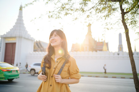 Traveler asian woman 30s stands bathed in the golden glow of sunset, embracing the freedom of exploration. on summer holiday weekend vacation trip in Bangkok, Thailandの写真素材