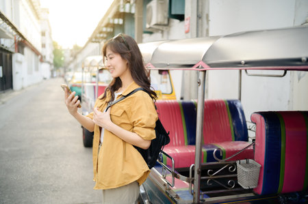 Asian Young woman backpack traveler standing a side of Tuk Tuk taxi on summer vacations at Bangkok, Thailand. Journey trip lifestyle, Asia summer tourism concept.の写真素材