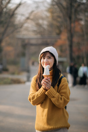 Happy lady in yellow sweater having fun with ice cream. Asian woman in a cute ethnic outfit, smiling and posing outdoors, creating a joyful and stylish lifestyle moment.の写真素材