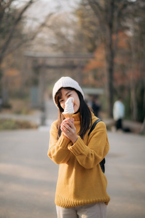 Fashionable woman in yellow sweater holding an ice cream cone. Smiling portrait of cute girl in an ethnic outfit, expressing joy and delight outdoors.の写真素材