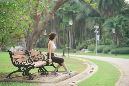 Woman jogger refreshing and sitting over bench in a park after runningの写真素材