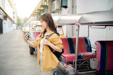 Asian Young woman backpack traveler standing a side of Tuk Tuk taxi on summer vacations at Bangkok,...