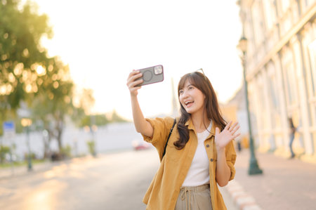 Traveler asian woman in her 30s making a livestream and selfie with a smartphone enjoying travel in Bangkok, Thailand. Journey trip lifestyle, world travel explorer or Asia summer tourism concept.の写真素材