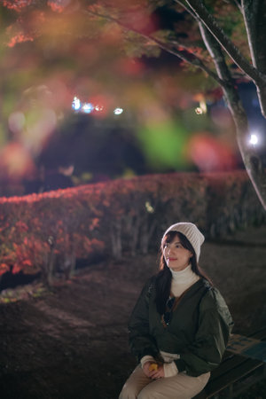 Woman in stylish jacket enjoys the holiday season in Kawaguchiko, surrounded by the beauty of nature and festive lights.の写真素材