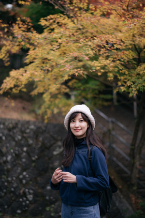 Asian woman in Japan's fall beauty, a cheerful holiday portrait in Kyoto. Vibrant foliage, friends, and smiles by lake create a joyful and scenic atmosphere.の写真素材