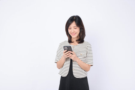 Southeast asian woman happily using mobile phone to access internet application in bright setting with casual striped jacket and black dressの写真素材
