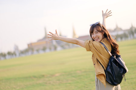 Happy southeast asian woman travel concept with open arms enjoying outdoor green field and bright daylight in joyful moment of freedom and adventureの写真素材