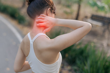 A sport activity in public park with southeast asian female teen jogging running for health experiencing pain during exercise holding her neck in discomfort outdoorsの写真素材