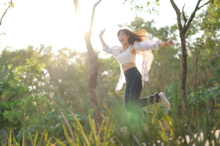 A southeast asian female young woman enjoying refreshing deep breath in public park showing wellness and healthy lifestyle with joyful energy in nature. cheerful young woman jumps joyfullyの写真素材