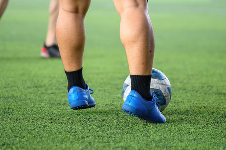 A soccer players in action during game on grass field focusing on their legs and ball, showing blue cleats and black socks in motion with blurred backgroundの写真素材