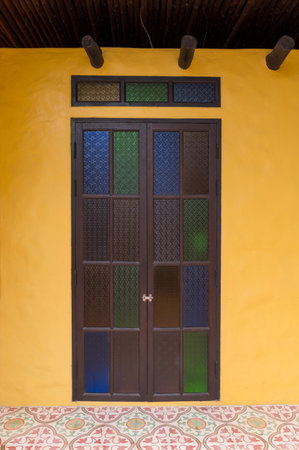 A twin door with colorful stained glass panes set in dark frame on vibrant yellow wall above patterned tile floor, creating charming and artistic architectural featureの写真素材