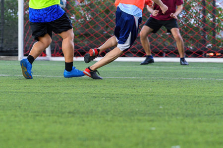 A soccer players in action on green grass field focusing on their legs and ball near goal net during intense gameの写真素材