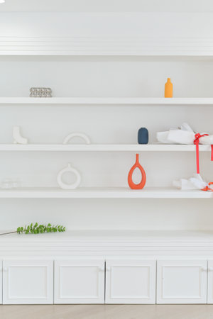 A minimalist white shelf featuring simple decor items including vases and decorative objects arranged in clean style with touch of color and greenery for fresh lookの写真素材
