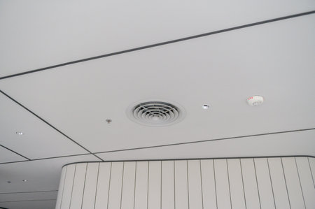A clean modern office ceiling featuring air vents, recessed lighting, and grid pattern with smooth...