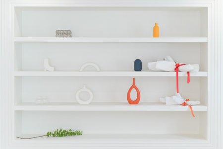 A minimalist white shelf featuring simple decor items including vases and decorative objects arranged in clean style with touch of color and natural greenery for calm atmosphereの写真素材