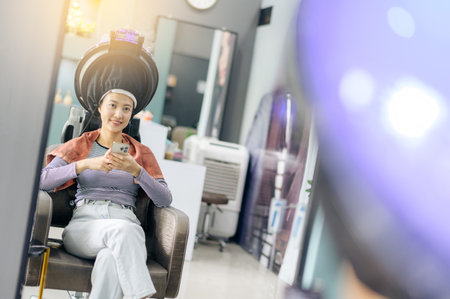 A happy young southeast asian female customer, young woman or girl, receives hair dyeing service process at salon providing beauty wellness healthcareの写真素材