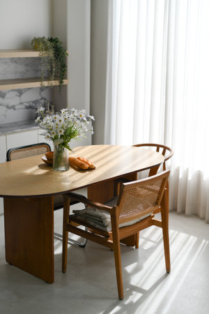 A peaceful interior room inside home features wooden dining table and cane chair bathed in soft...