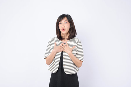 A surprised southeast asian woman with medium length black hair wearing striped jacket and black dress standing against white background with expressive faceの写真素材