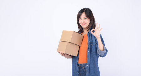 A southeast asian woman holding cardboard boxes shows ok gesture while enjoying internet online...