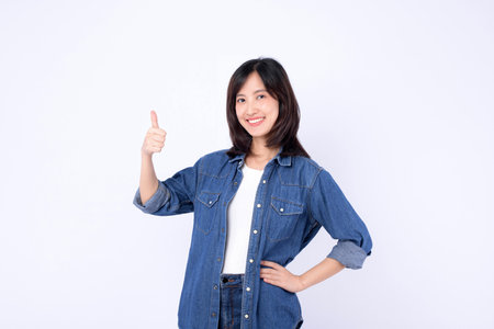 A southeast asian woman in casual denim shirt smiling and showing thumbs up gesture with confidence and positivity on white backgroundの写真素材