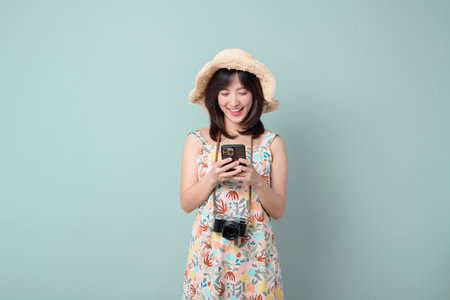 A southeast asian woman wearing summer dress and straw hat smiling while using smartphone with...