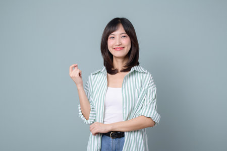 A smiling young asian businesswoman standing confidently, wearing white and green shirt, casual style, over green backgroundの写真素材