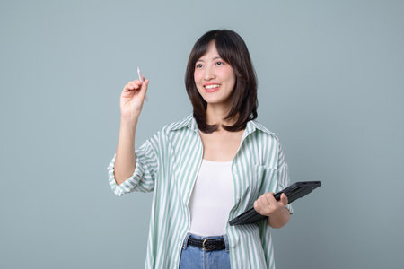 A southeast asian woman holding tablet and stylus smiling while using internet technology for creative work against plain backgroundの写真素材
