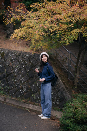 A southeast asian woman travel in autumn park wearing casual clothes and hat smiling happily near...