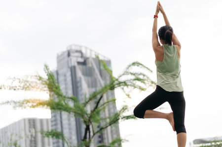 A focused asian woman in an urban city at sunset wellness fitness yoga workout with stretching exercise reduces medical shoulder pain muscle strain inflammation and lowers injury risk for healthcareの写真素材