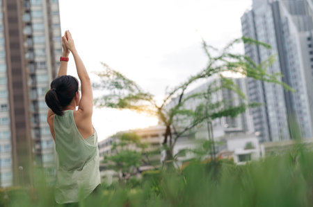 An asian woman enjoys sunset fitness yoga workout. stretching exercise reduces medical injury risk like shoulder pain inflammation or muscle strain promoting wellness and healthcare in an urban cityの写真素材