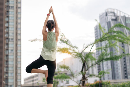 Asian woman in 30s fitness yoga workout. Stretching exercise reduces medical injury risk shoulder pain muscle strain inflammation. Healthy lifestyle wellness healthcare in urban city at sunsetの写真素材