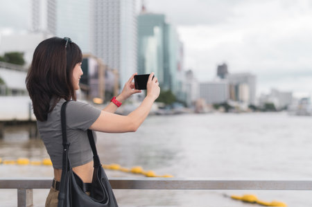 A solo southeast asian woman teenager blogger world travel tourism experience bangkok thailand. she wait for boat chao phraya river and take photo with smartphone to express local cultural conceptの写真素材