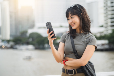A young southeast asian woman happy teenager blogger using smartphone searching travel guide. world explorer asia tourism concept with local cultural experience near chao phraya river bangkokの写真素材