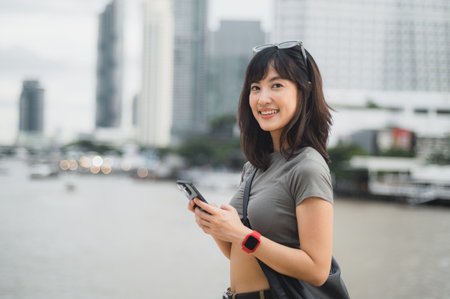 A happy young southeast asian woman teenager blogger using smartphone for searching travel guide. world explorer enjoying local cultural experience. asia tourism concept chao phraya river bangkokの写真素材