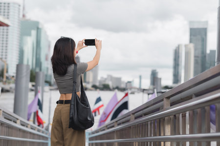 A solo southeast asian woman teenager blogger world travel explorer take photo smartphone express local cultural experience tourism concept wait boat chao phraya river bangkok thailand asiaの写真素材