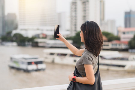 A solo southeast asian woman teenager blogger on world travel tourism. happy explorer take photo with smartphone of boat on chao phraya river. local cultural experience in bangkok thailand asiaの写真素材