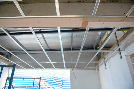 A focused interior renovation shows installation of an aluminium ceiling framework with exposed electrical wiring. complex process is part of home improvement projectの写真素材