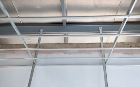 A hopeful progress of interior renovation with aluminium ceiling framework. electrical wiring installation reveals complex grid system during home improvement projectの写真素材