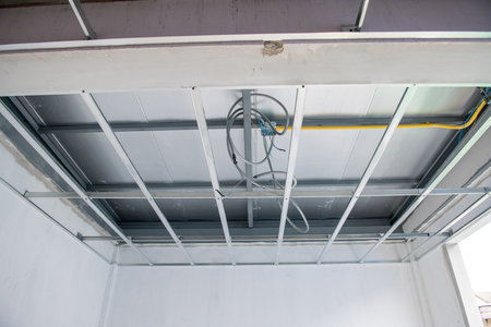 An interior renovation work showing new aluminium ceiling framework and complex electrical wiring during installation phase. focused view on building construction progressの写真素材