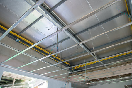 A focused view of an interior renovation showing ceiling framework installation. exposed electrical wiring runs alongside new aluminium panels during house construction projectの写真素材